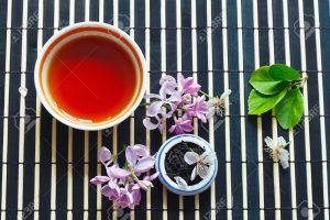 13590434-Cup-of-tea-jar-of-tea-leaves-and-cherry-blossoms-and-leaves-with-lilac-on-bamboo-table-cloth-still-l-Stock-Photo